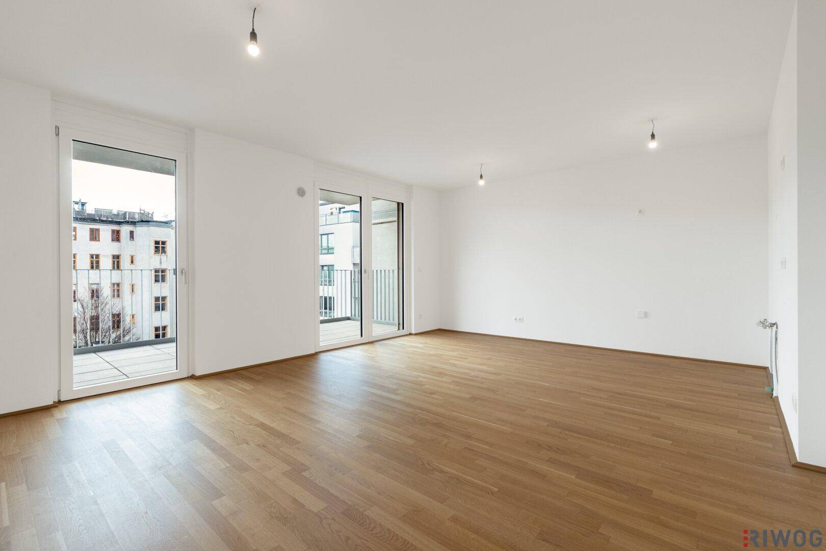 Helles Wohnzimmer mit Parkettboden und Zugang zu zwei Balkonen, bietet viel Tageslicht und Flexibilität.