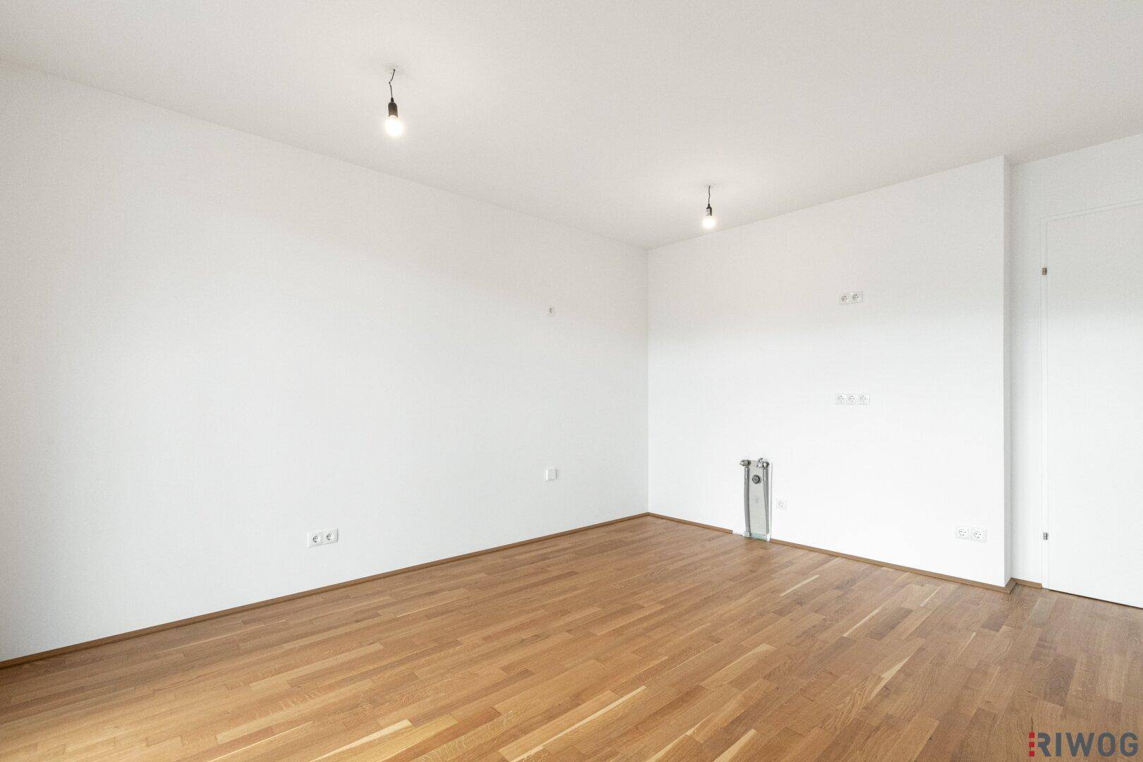 Leerer Raum mit hellem Parkettboden und weißen Wänden, ideal für Wohn- oder Essbereich.