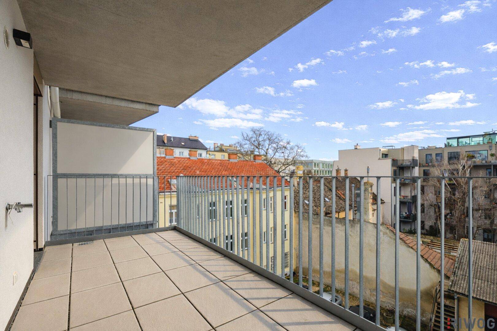 Heller Balkon mit Fliesenboden und Blick auf die umliegenden Gebäude und Dächer der Stadt.