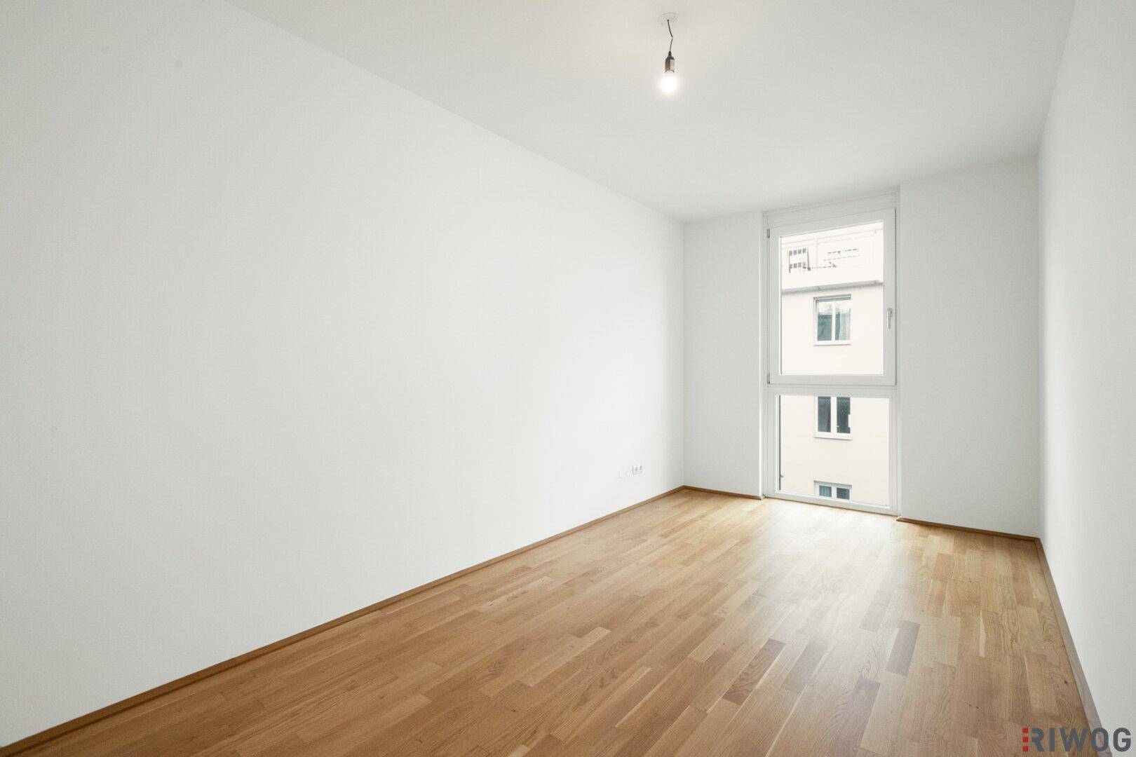 Leeres Zimmer mit Parkettboden und großem Fenster, vielseitig nutzbar als Schlaf- oder Arbeitszimmer.