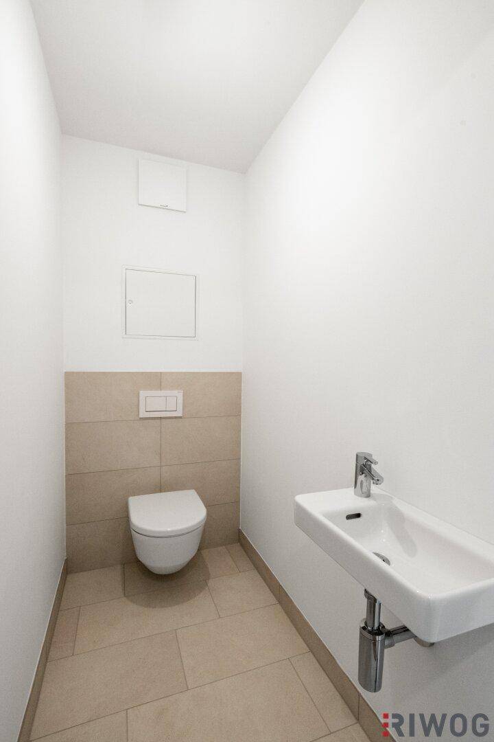 Helles Gäste-WC mit Wand-WC und kleinem Waschbecken, modern gefliest und funktional.