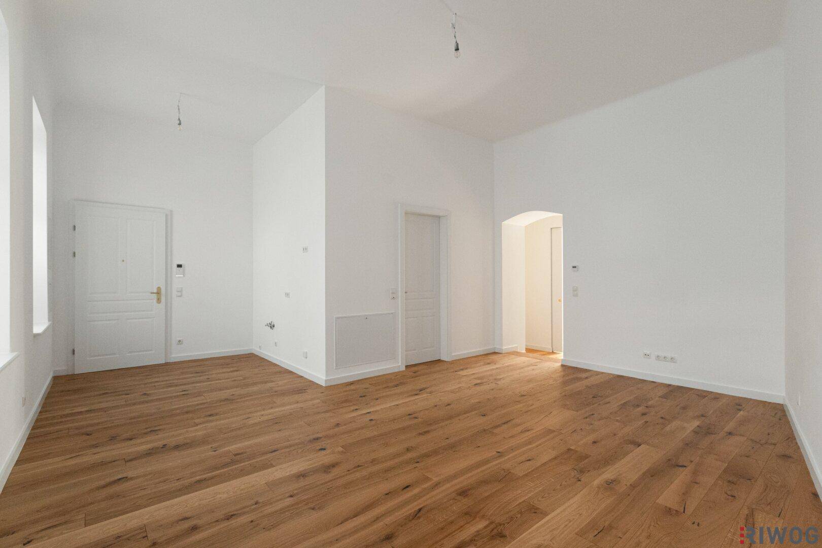 Helles, leeres Zimmer mit Holzboden und weißen Wänden, bereit zur individuellen Gestaltung.