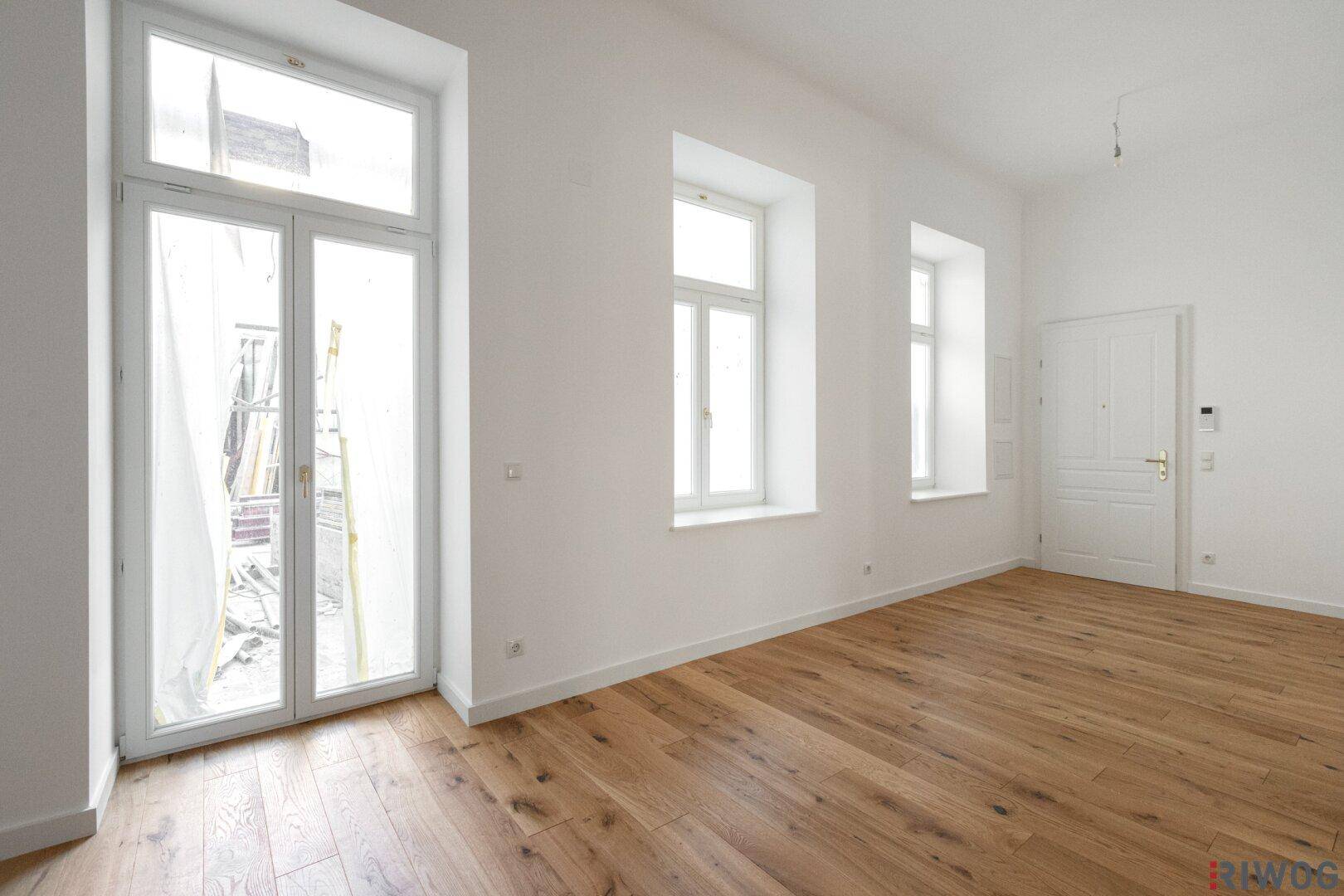 Lichtdurchfluteter Raum mit hohen Fenstern und elegantem Holzboden, ideal für ein Wohnzimmer.