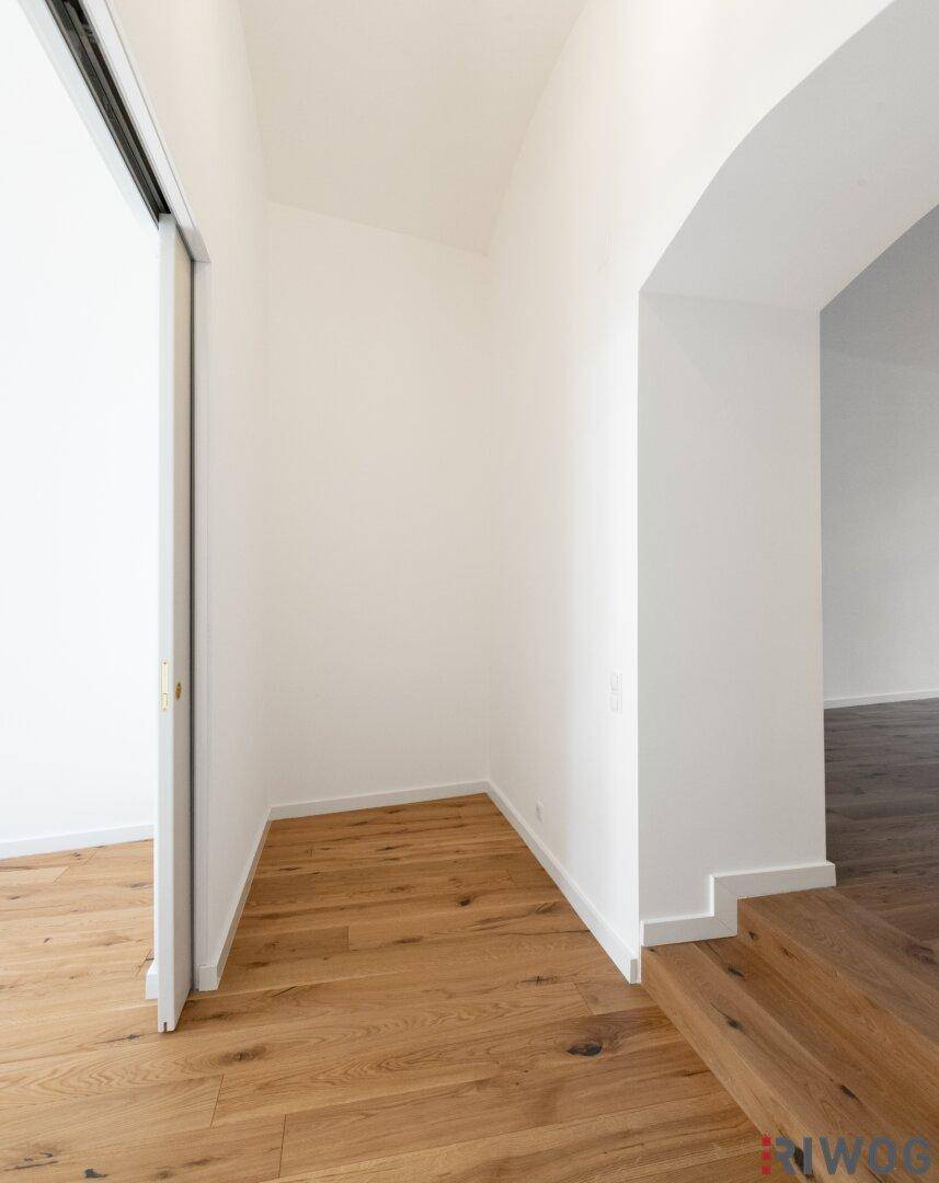 Heller Flur mit Holzboden und einem eleganten Bogen, der zu einem weiteren Raum führt.