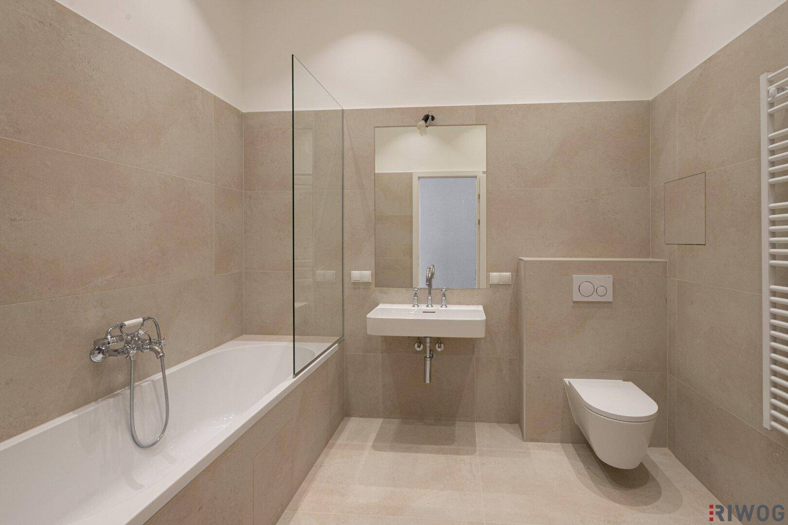 Modernes Badezimmer mit Badewanne, Dusche, WC und beigefarbenen Fliesen an Wänden und Boden.