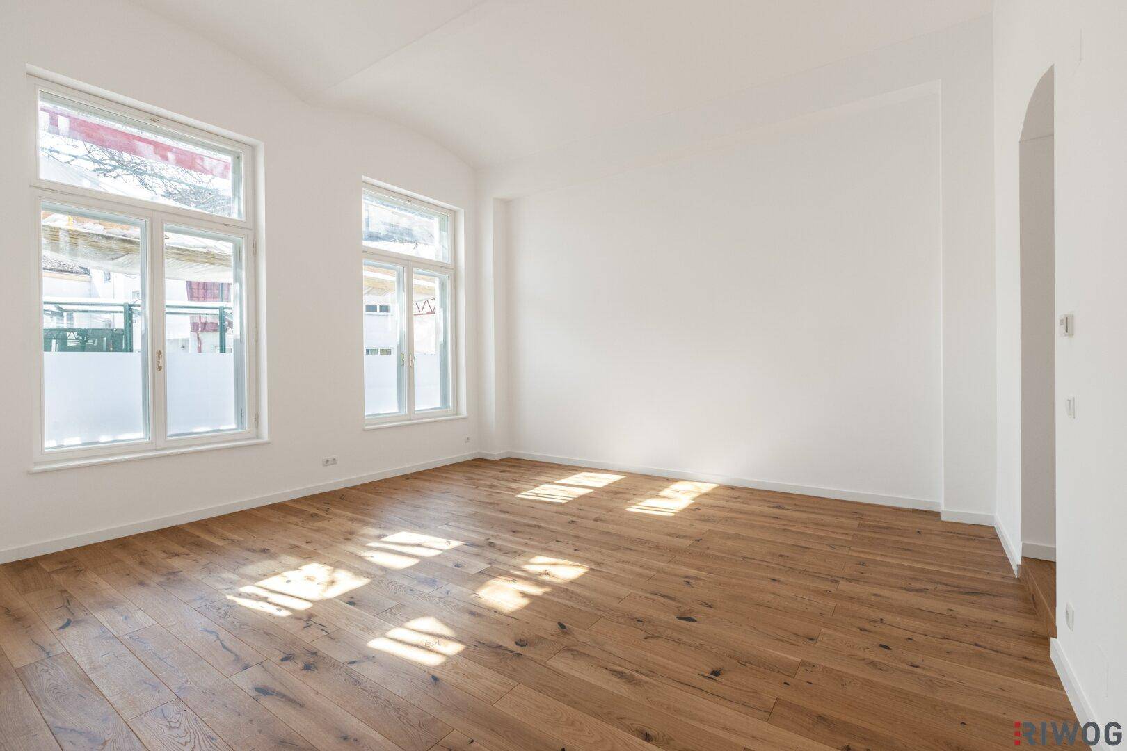 Geräumiger, heller Raum mit Holzboden und großen Fenstern, bereit zur individuellen Einrichtung.