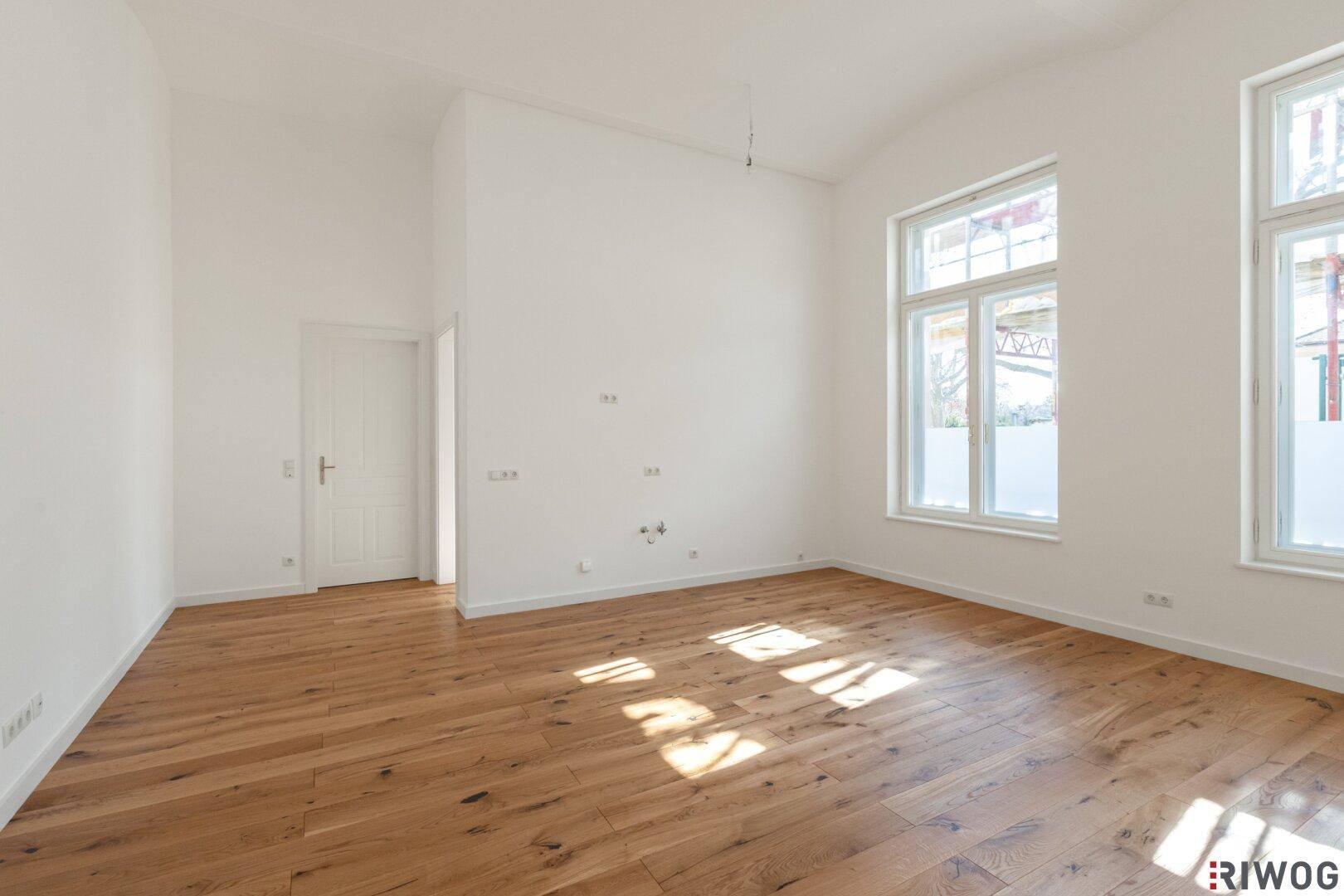 Leerer Raum mit Holzboden, hohen Decken und weißer Tür, ideal für vielfältige Nutzungsmöglichkeiten.