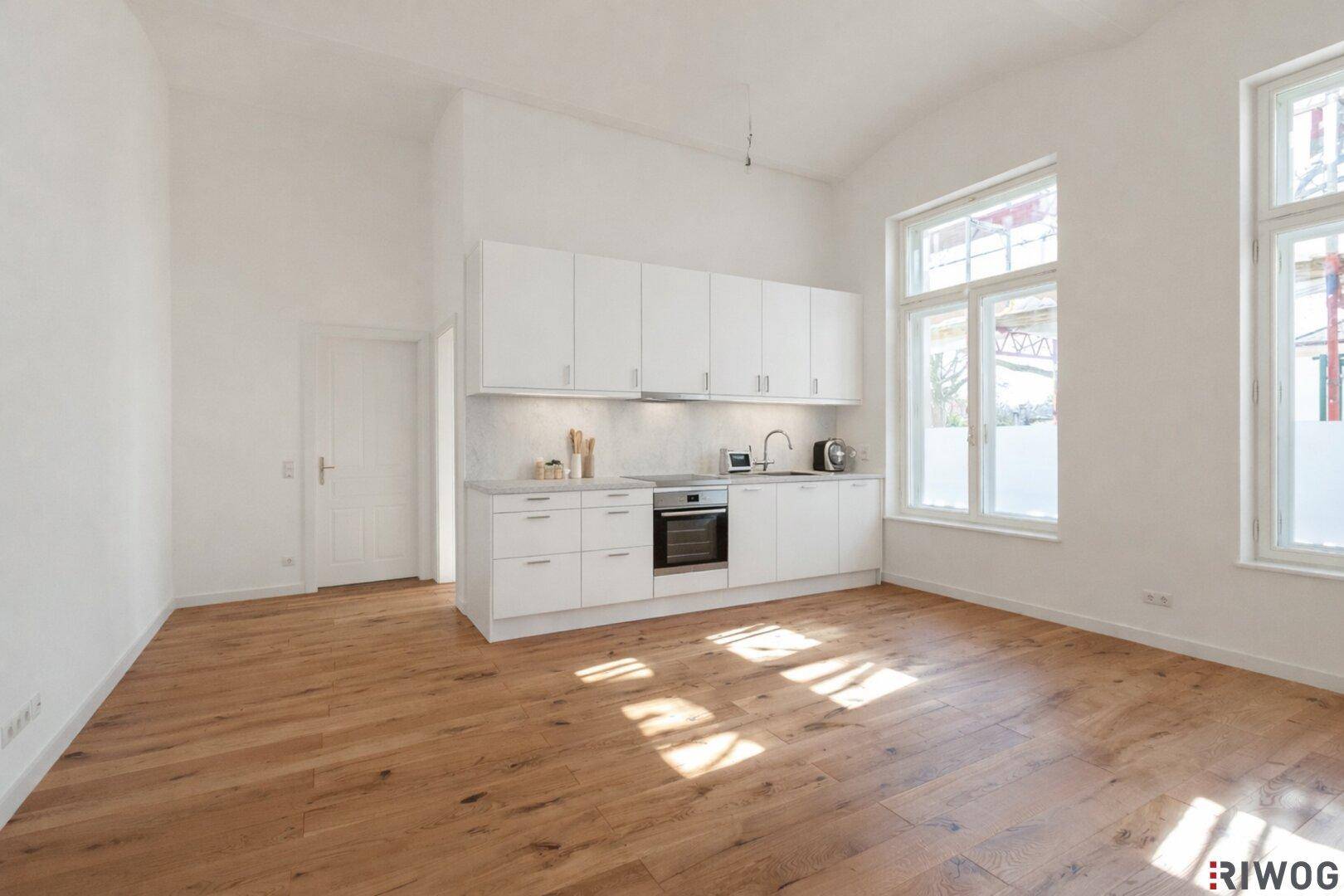Heller Raum mit neuer Einbauküche, Holzboden und großen Fenstern, bereit zum Kochen.