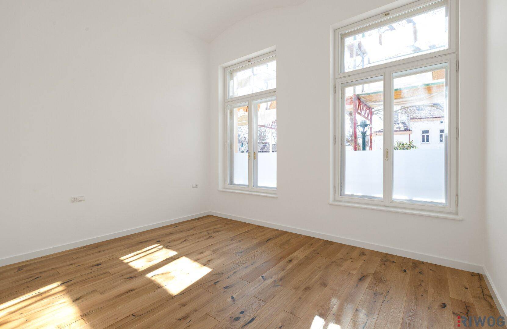 Unmöblierter Raum mit Holzboden und großen Fenstern, vielseitig nutzbar als Schlaf- oder Arbeitszimmer.