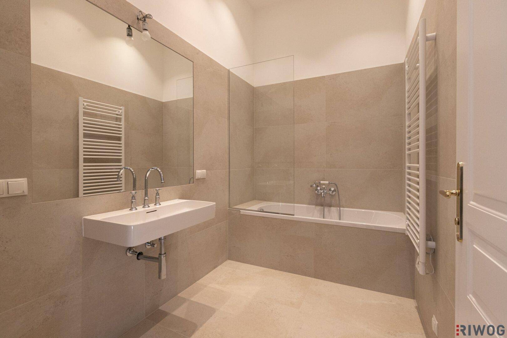 Modernes Badezimmer mit Badewanne, großem Spiegel und beigen Fliesen, in sehr gutem Zustand.