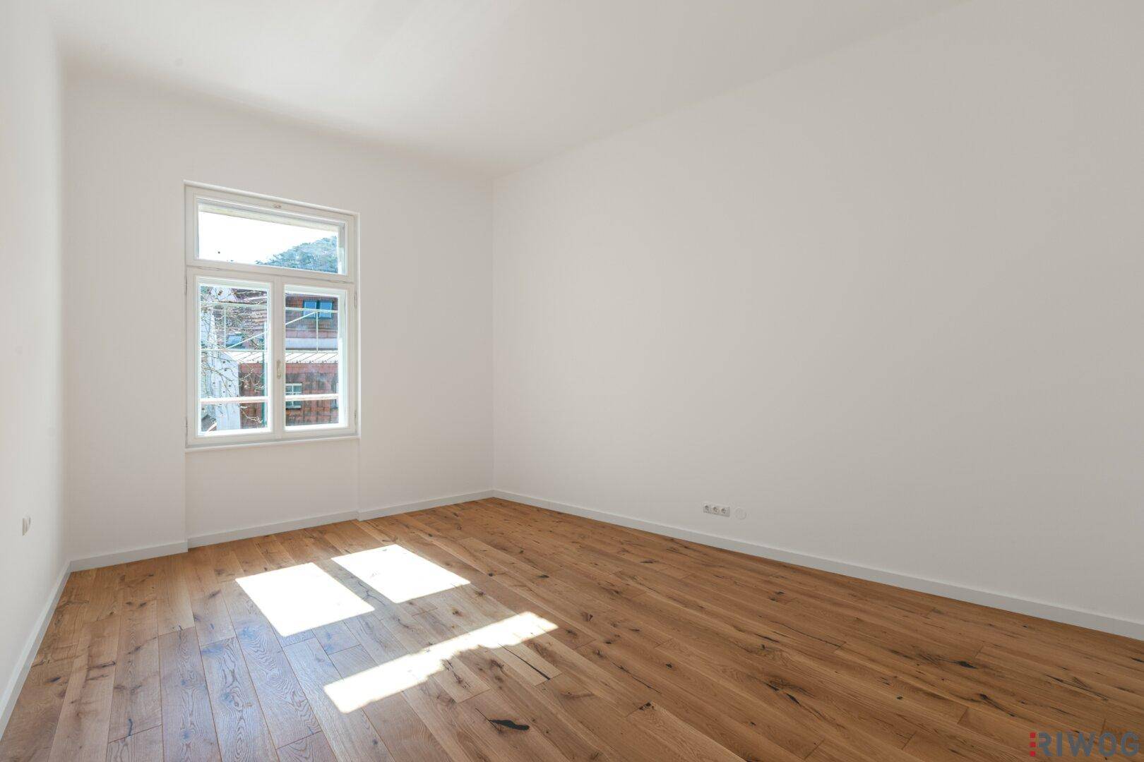 Helles, unmöbliertes Zimmer mit Holzboden und großem Fenster, ideal als Schlafzimmer.