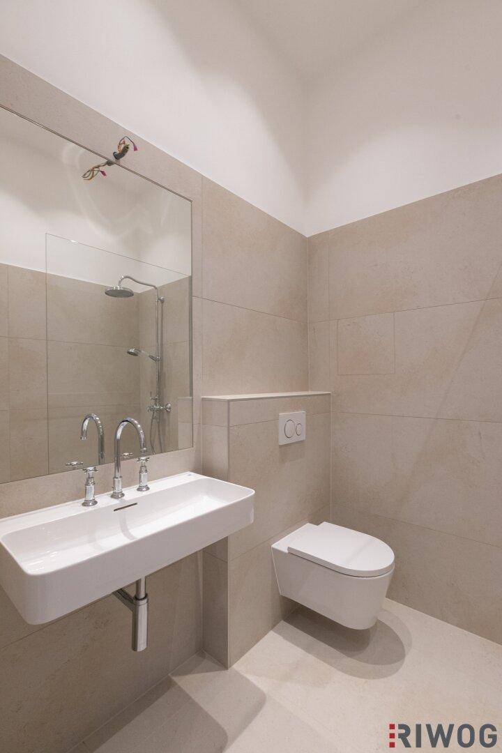 Modernes Badezimmer mit beigen Fliesen, wandhängendem WC und Einzelwaschbecken.
