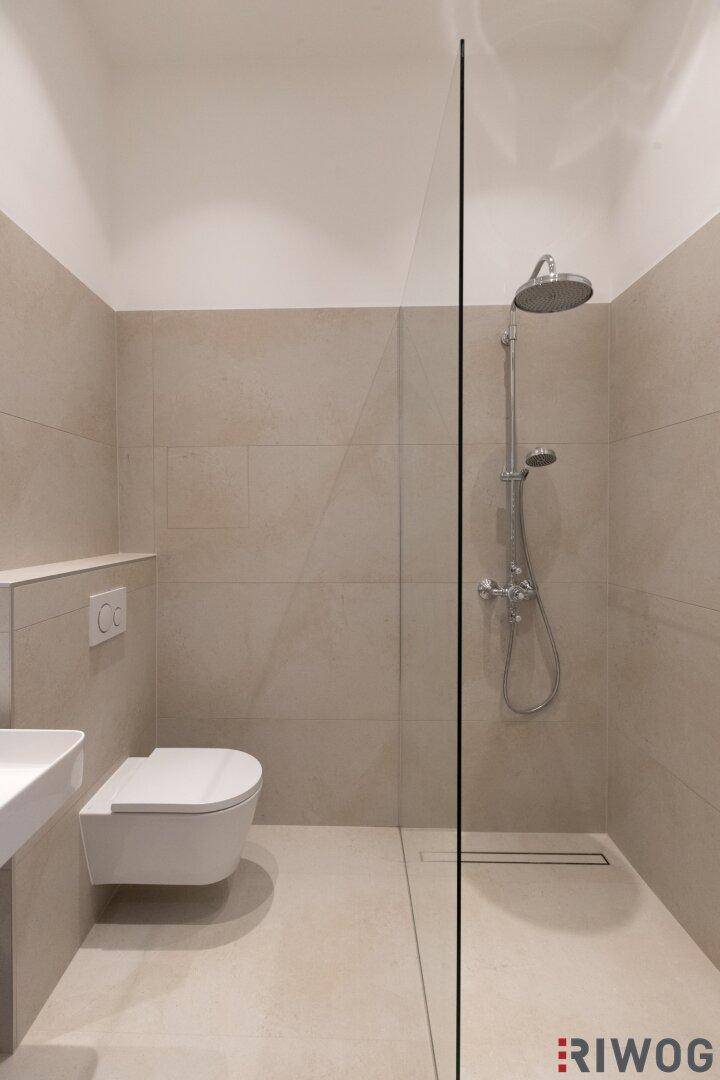 Begehbare Dusche mit Glaswand und Regenduschkopf in einem modernen Badezimmer.