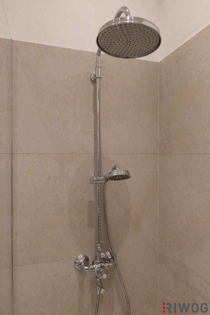 Detailansicht eines modernen Regenduschkopfs und Handbrause in einem gefliesten Bad.