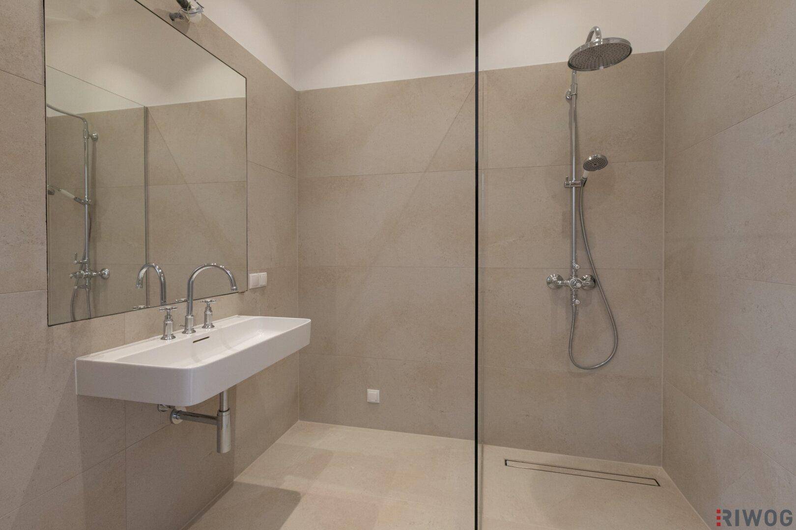Modernes Badezimmer mit begehbarer Dusche, großem Spiegel und beigefarbenen Fliesen.