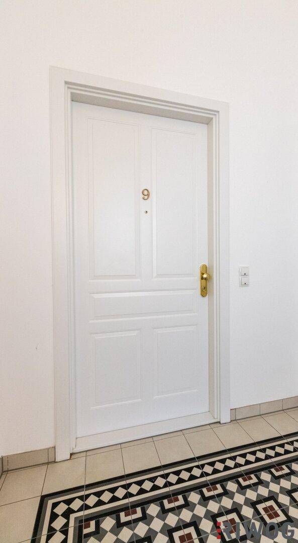 Weiße Wohnungstür mit goldener Nummer "9" und klassischem Fliesenboden im Eingangsbereich.
