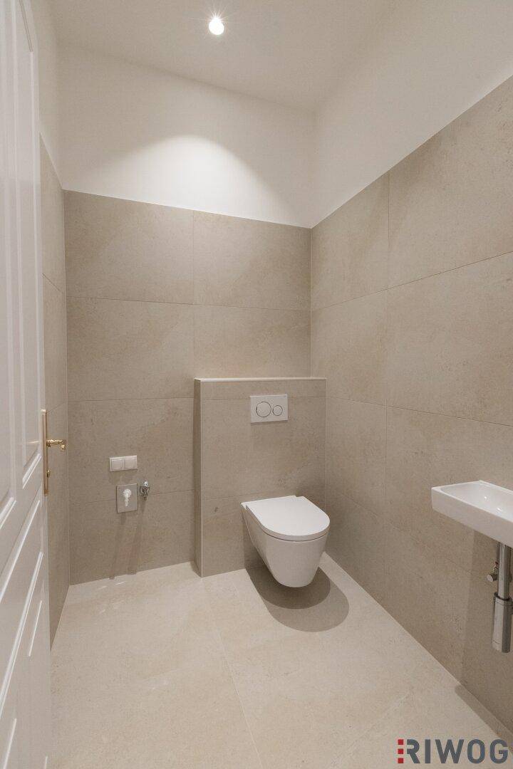 Modernes Gäste-WC mit wandhängender Toilette und kleinem Waschbecken, in hellen Beigetönen gehalten.