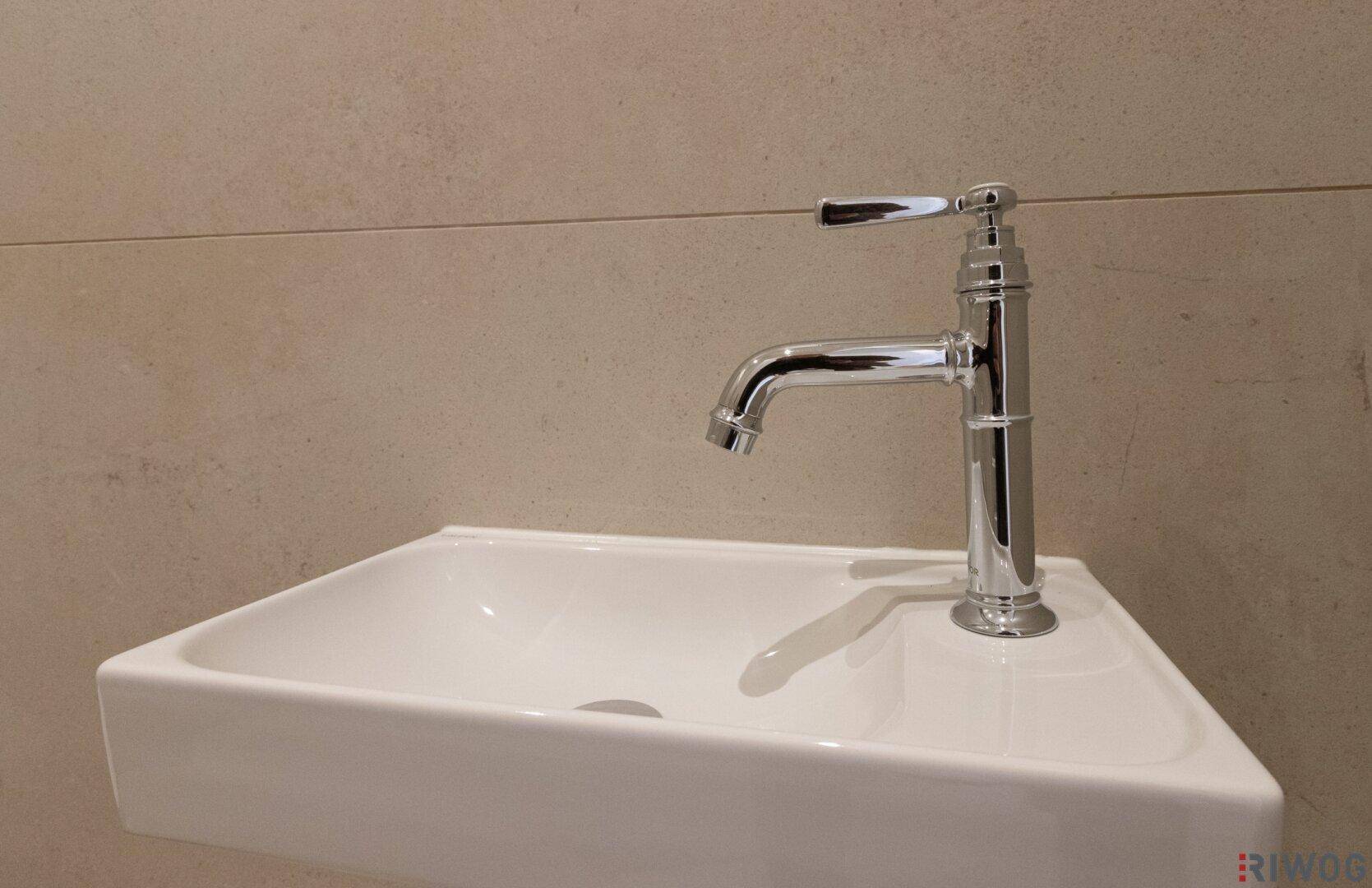 Detailaufnahme eines modernen Waschbeckens mit stilvollem Chromwasserhahn und beigefarbenen Fliesen.