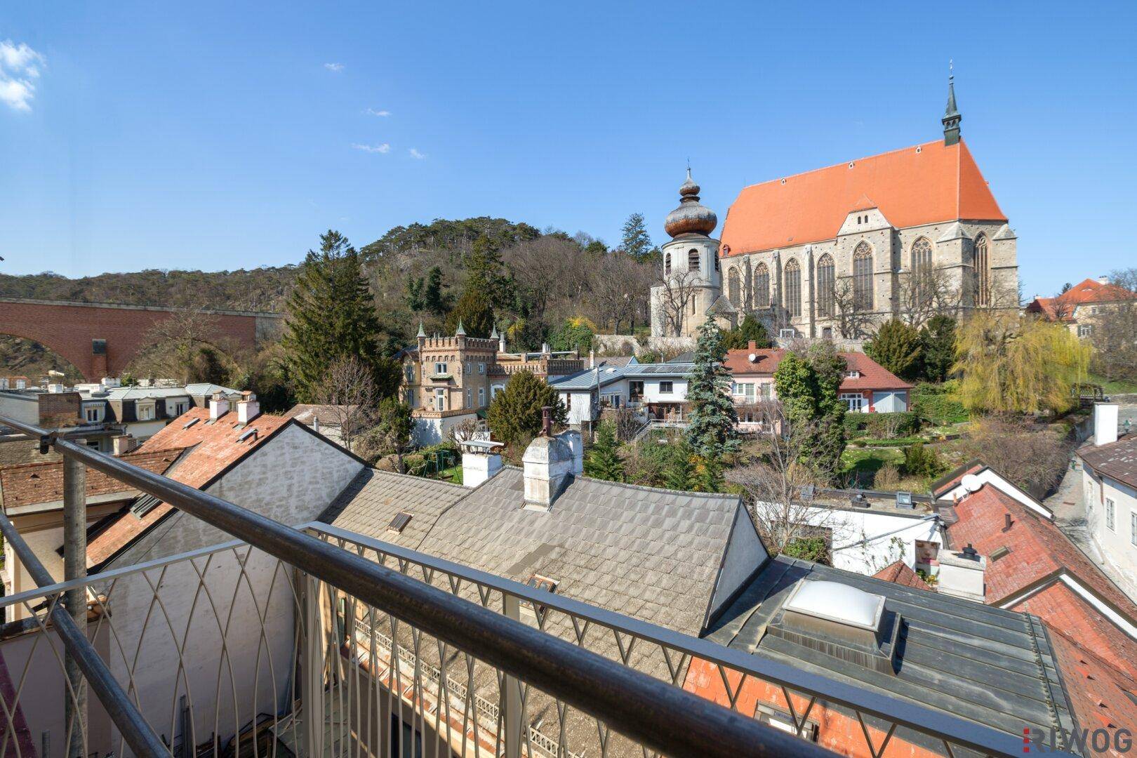 Sonniger Balkon mit Blick auf eine historische Stadtkulisse und eine imposante Kirche.