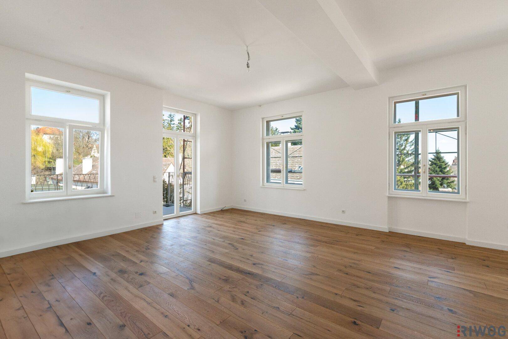 Geräumiges, helles Zimmer mit Holzboden und Zugang zu einem französischen Balkon, ideal für Wohnzwecke.