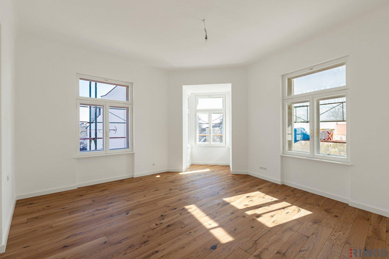 Helles, leeres Zimmer mit Erkerfenstern und Holzboden, ideal als Schlaf- oder Arbeitszimmer.