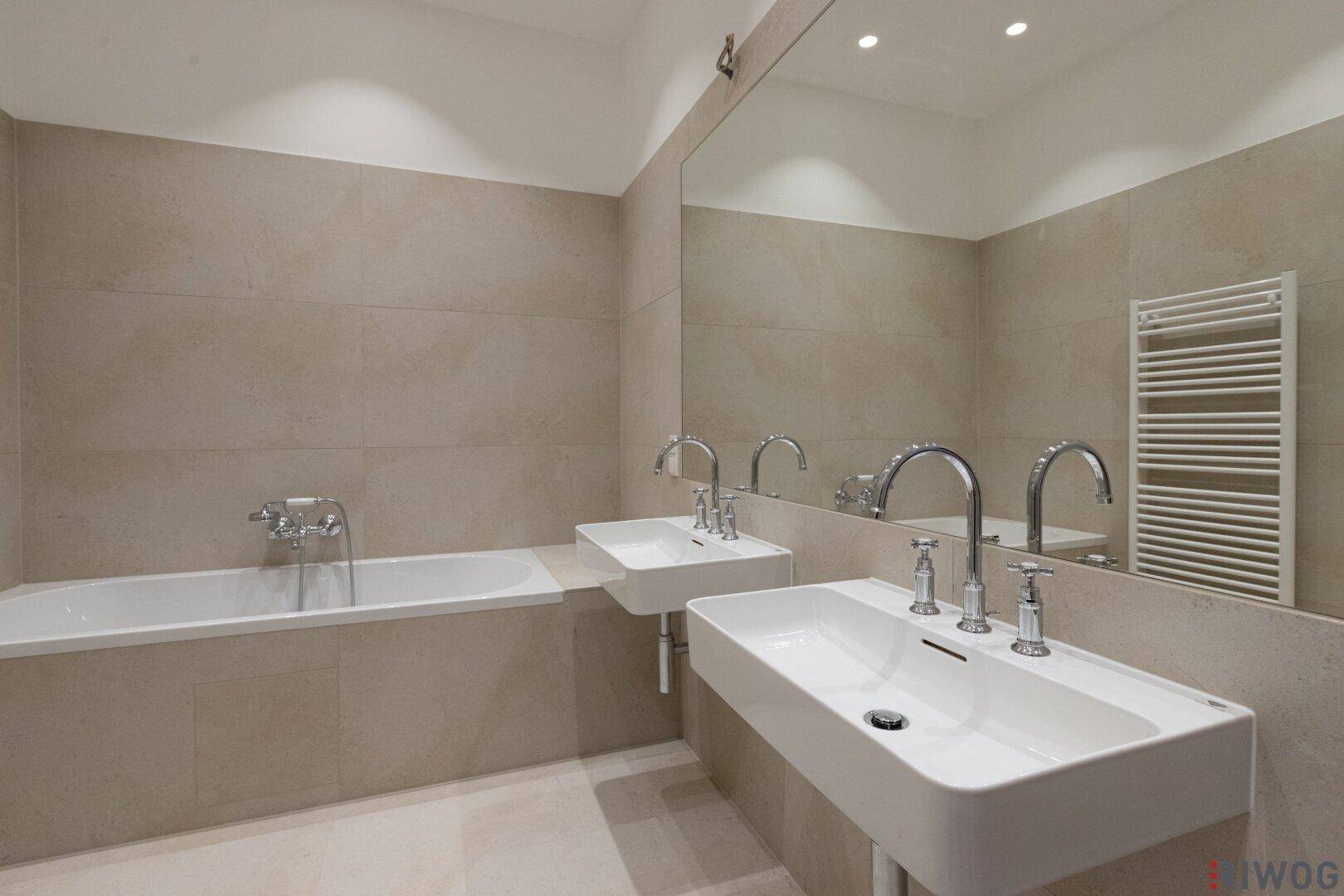 Elegantes Badezimmer mit Badewanne, Doppelwaschbecken und großem Spiegel, in hellen Farbtönen gehalten.