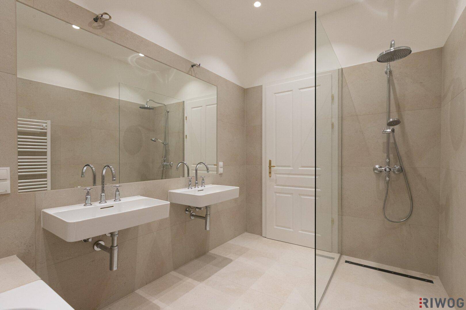 Modernes Badezimmer mit Doppelwaschbecken, großer Dusche und beigefarbenen Fliesen.