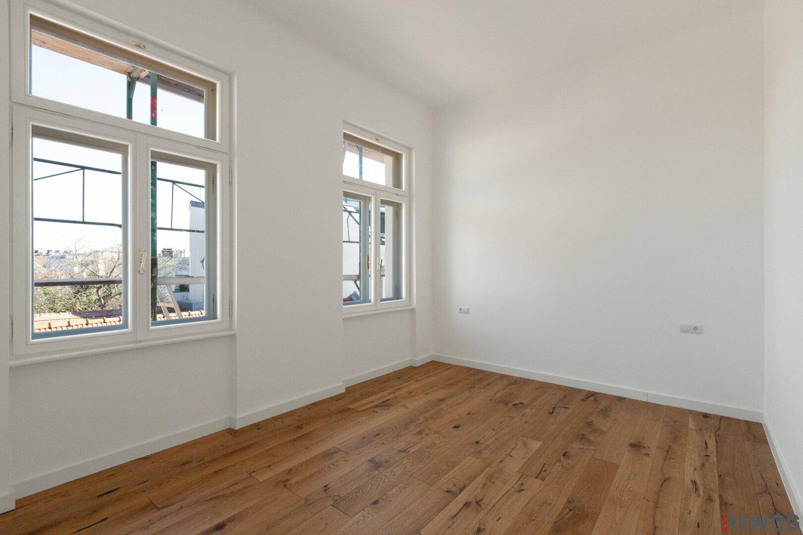 Helles, leeres Zimmer mit großen Fenstern und Holzboden, vielseitig nutzbar.