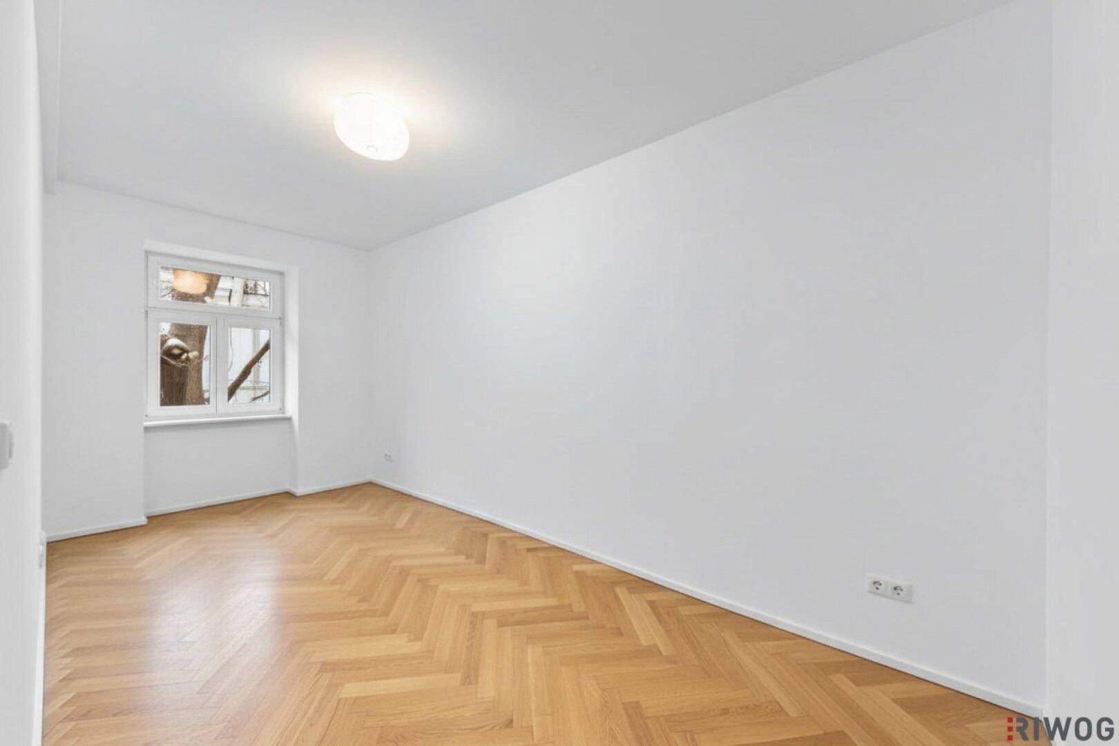 Leerer Raum mit Parkettboden und einem Fenster, bereit zur individuellen Gestaltung.