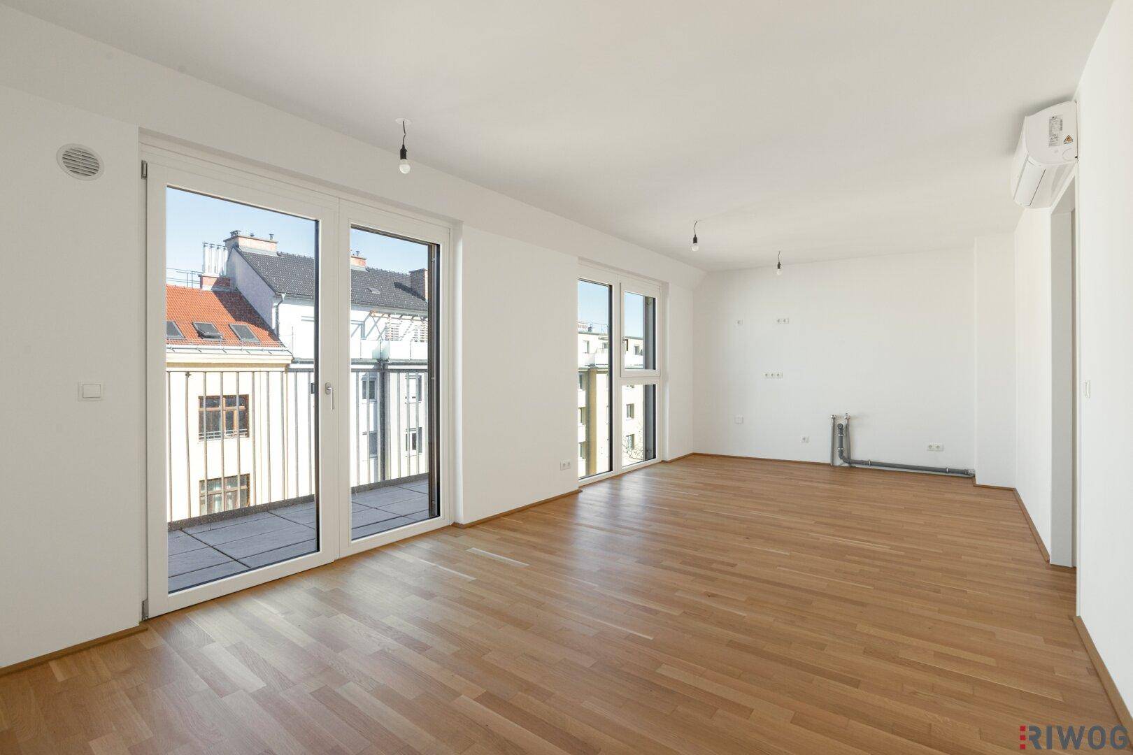 Geräumiges Wohnzimmer mit Holzboden, großen Fenstern und viel Tageslicht.