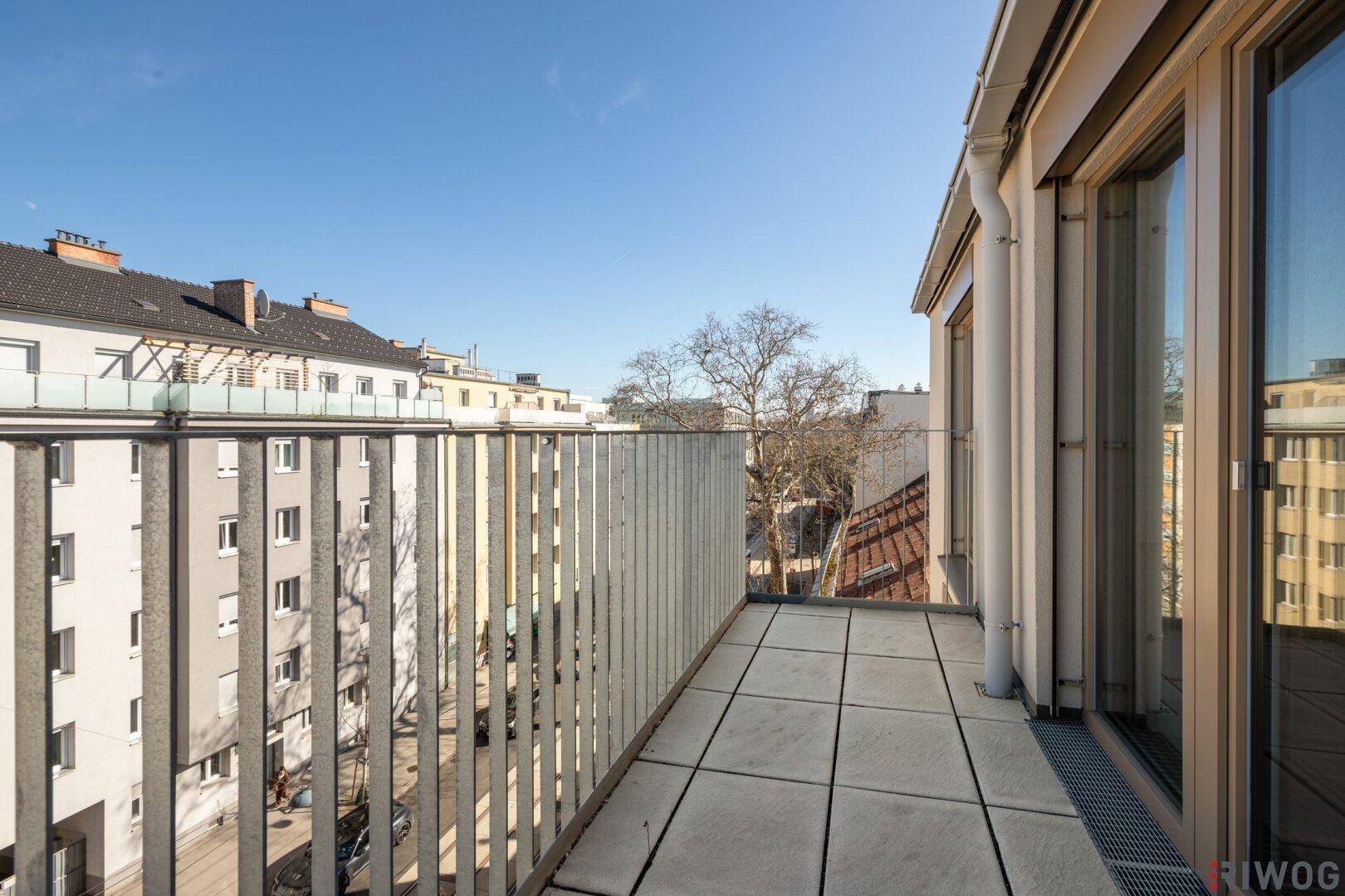 Heller Balkon mit Fliesenboden und Blick auf die umliegenden Gebäude und die Straße.