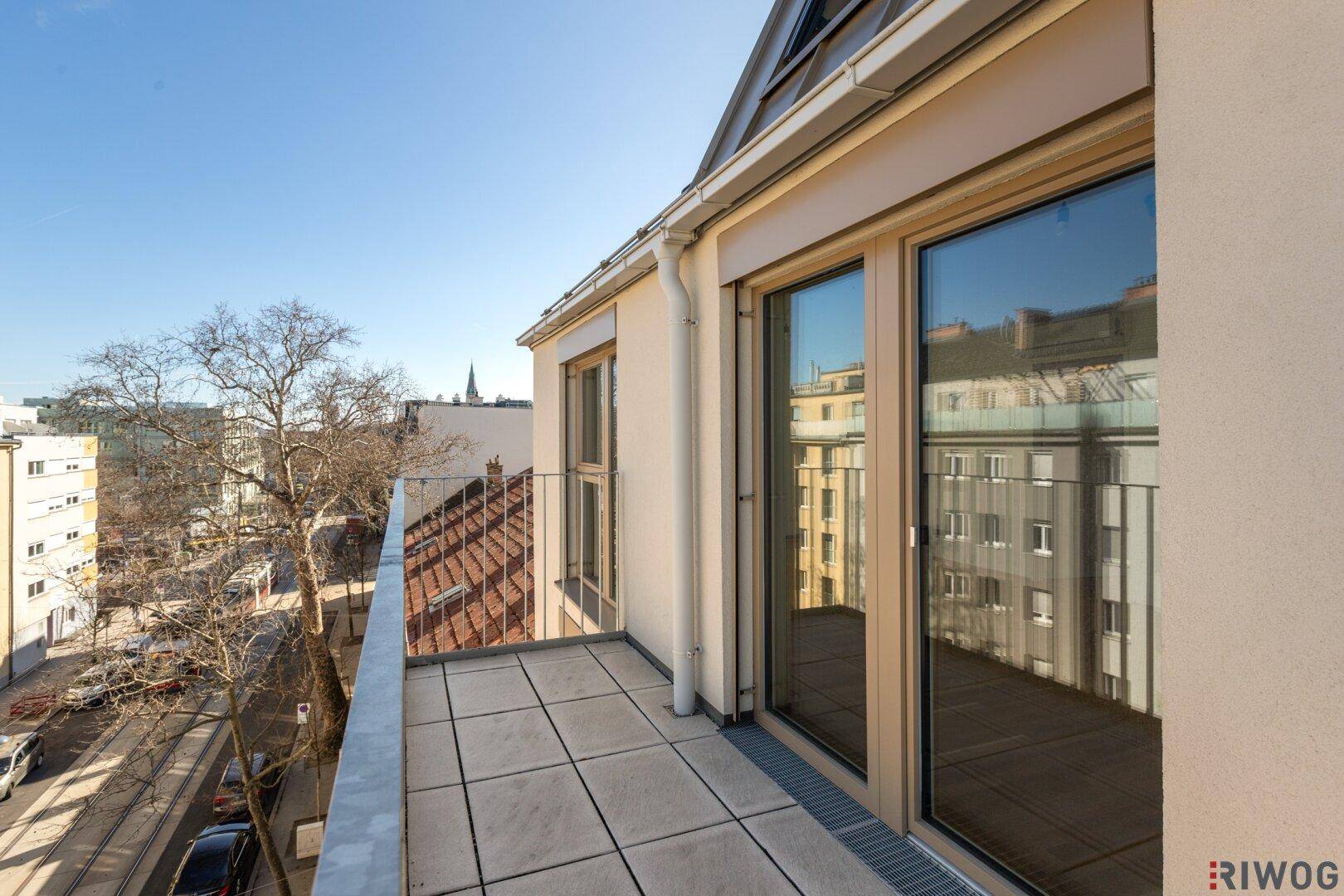 Geräumiger Balkon mit Fliesenboden und Blick auf die städtische Umgebung an einem sonnigen Tag.