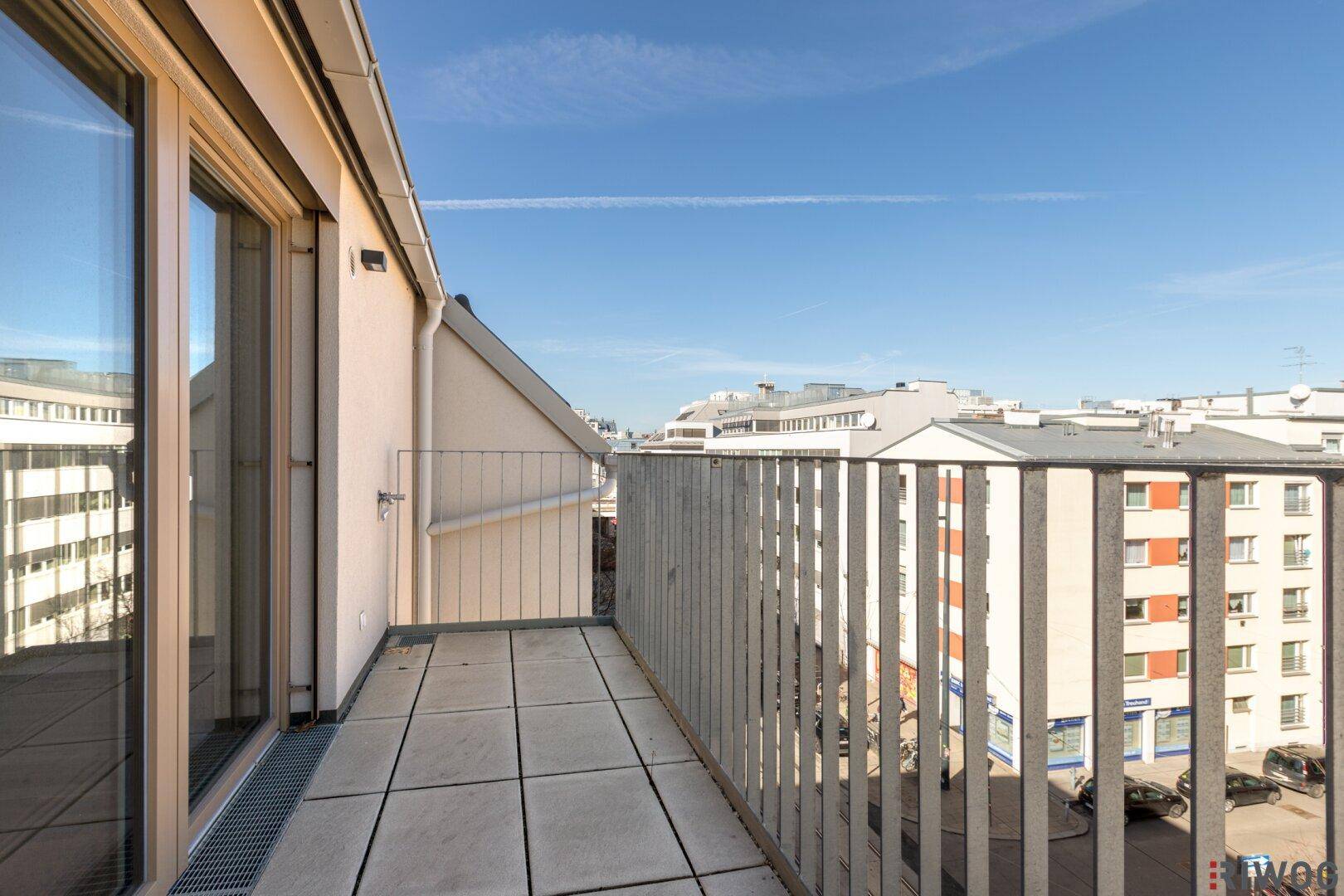 Langer Balkon mit Metallgeländer und Fliesenboden, bietet einen weiten Blick über die Stadt.