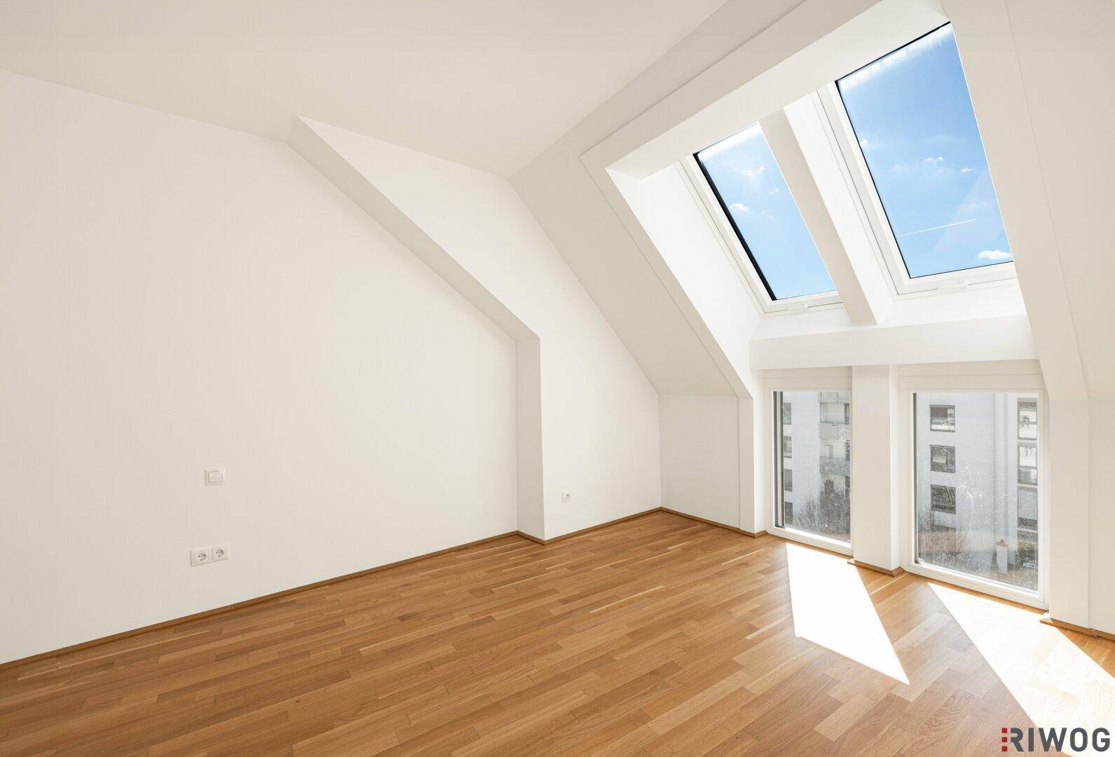 Helles Zimmer im Dachgeschoss mit Holzboden, Dachschrägen und großen Dachfenstern.
