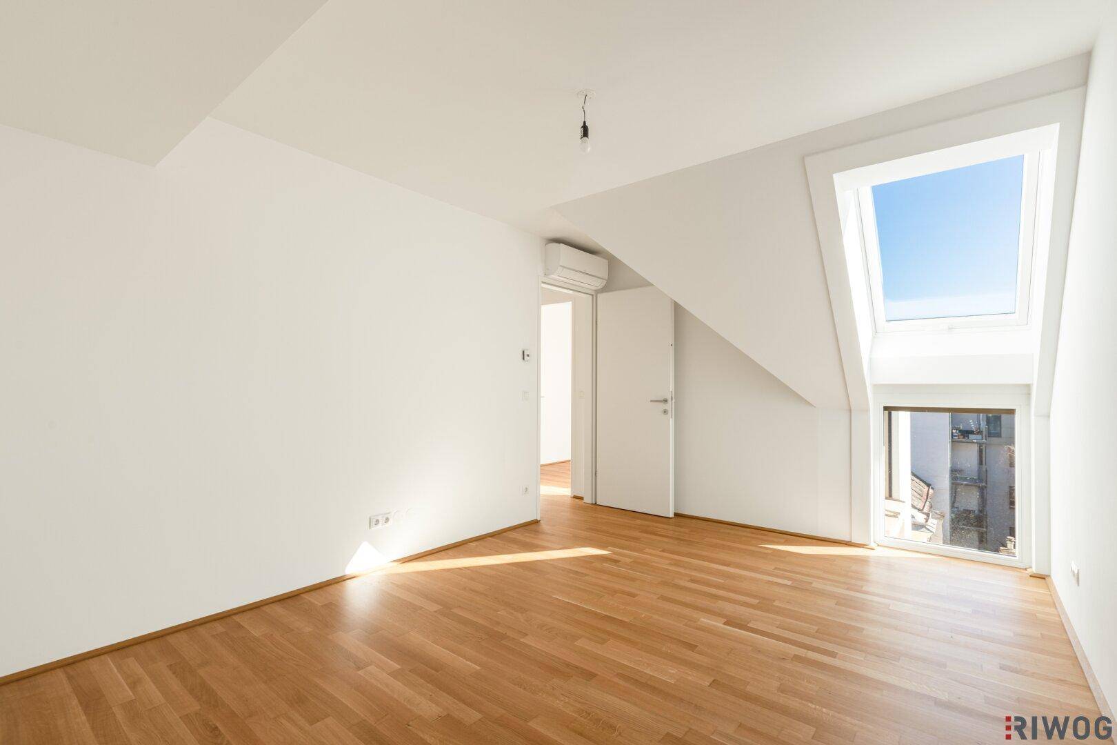 Lichtdurchflutetes Dachzimmer mit Parkettboden, Dachfenster und Klimaanlage.