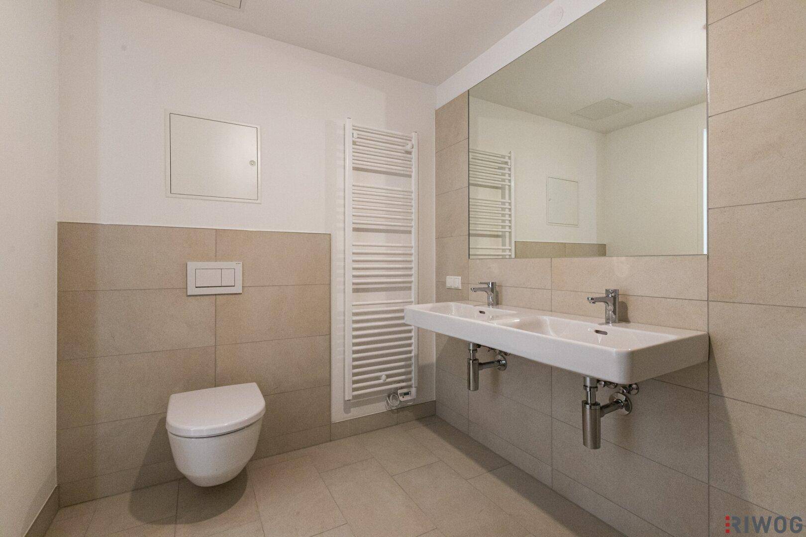 Zeitgemäßes Badezimmer mit Wand-WC, Doppelwaschbecken und großem Spiegel.
