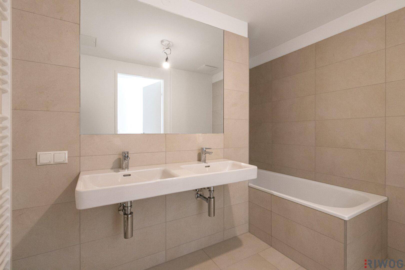 Modernes Badezimmer mit Doppelwaschbecken, Badewanne und beigefarbenen Fliesen.