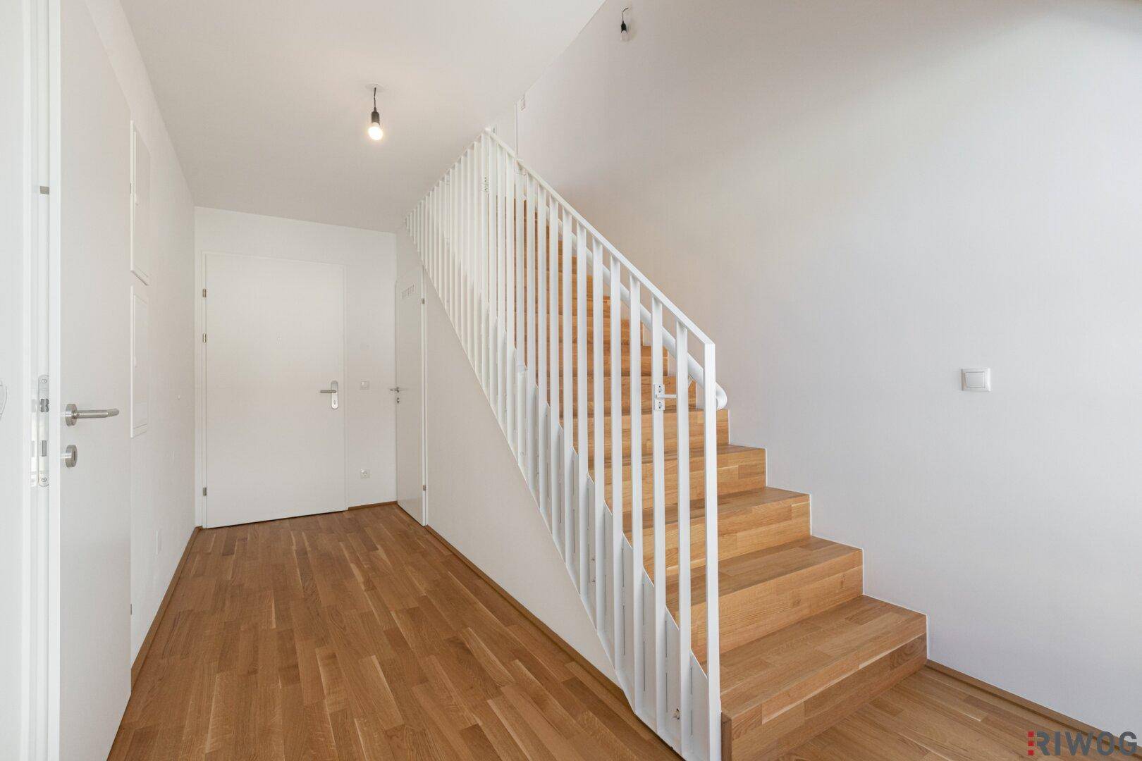 Heller Eingangsbereich mit Holztreppe, Holzboden und weißen Wänden.