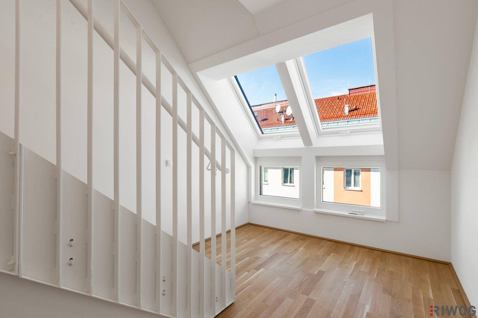 Heller Flurbereich mit Holztreppe, Dachfenstern und Blick auf die roten Dächer.