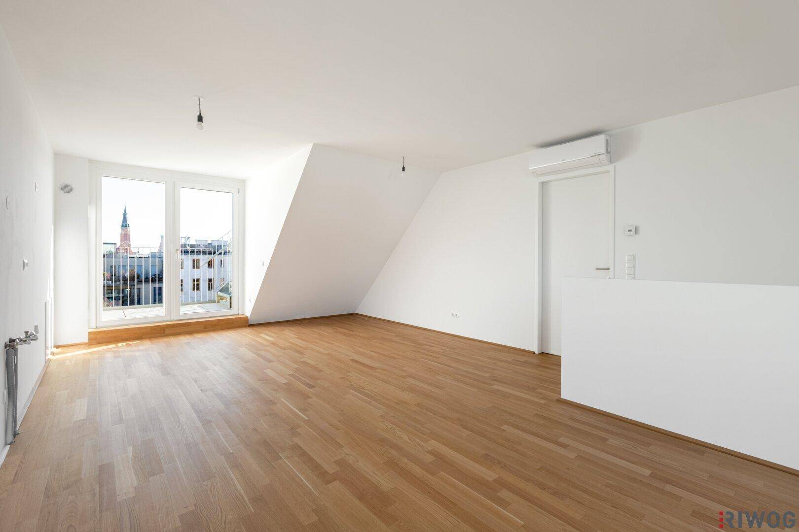 Heller Wohnraum mit Holzboden, Dachschräge und Zugang zu einem französischen Balkon.