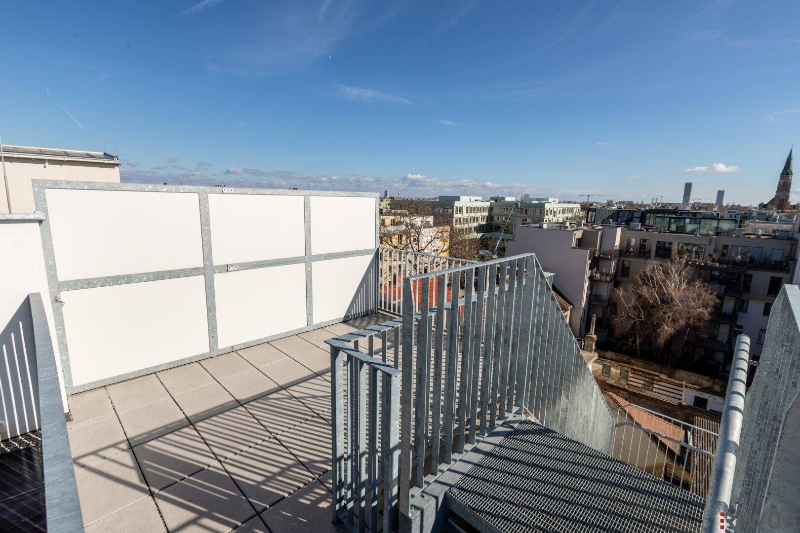 Unmöblierte Dachterrasse mit weitem Blick über die Dächer der Stadt an einem sonnigen Tag.