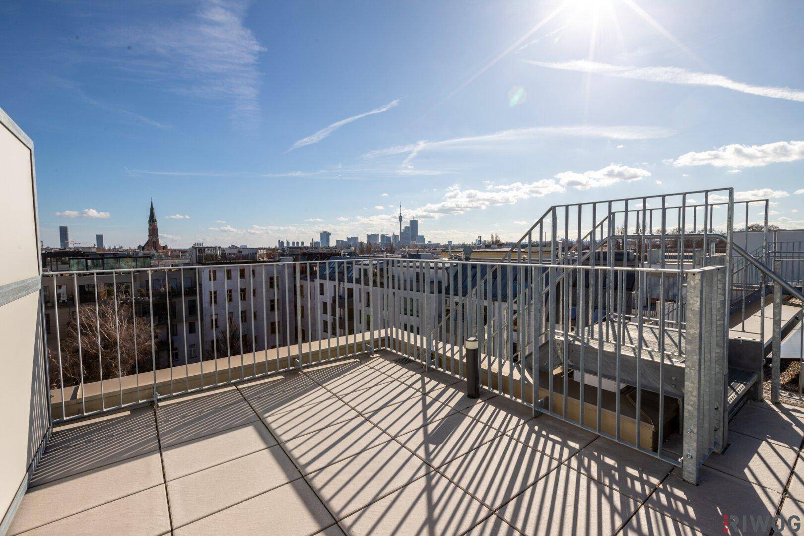 Geräumige Dachterrasse mit Metallgeländer und weitem Blick über die Stadt bei Tag.