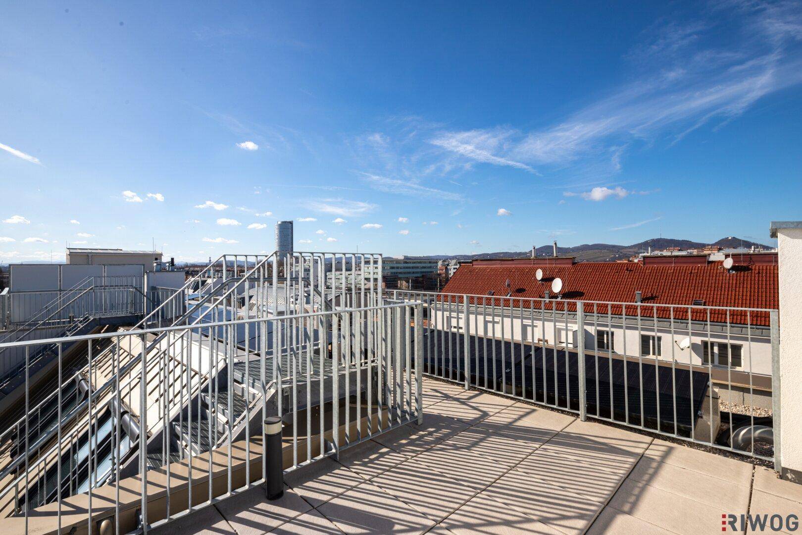 Geräumige Dachterrasse mit Blick auf die umliegende Stadtlandschaft und Berge im Hintergrund.