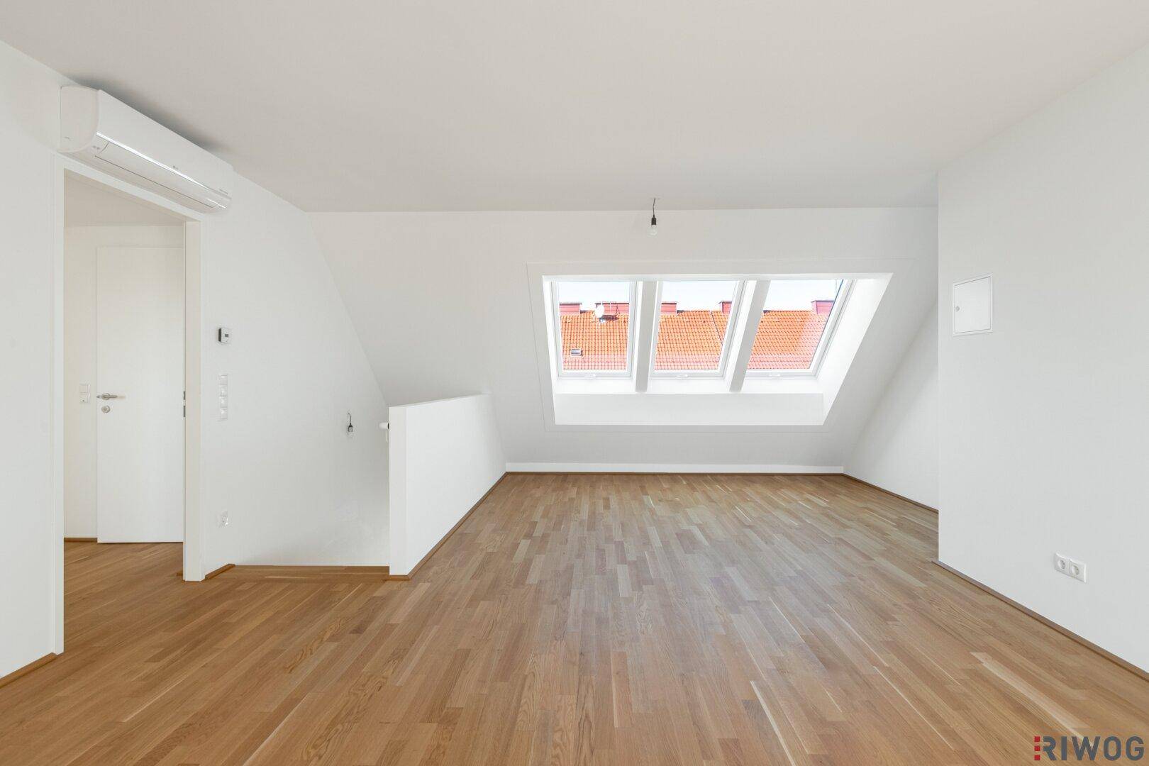 Geräumiger Wohnbereich mit Holzboden, Dachschräge, Klimaanlage und Dachfenstern.