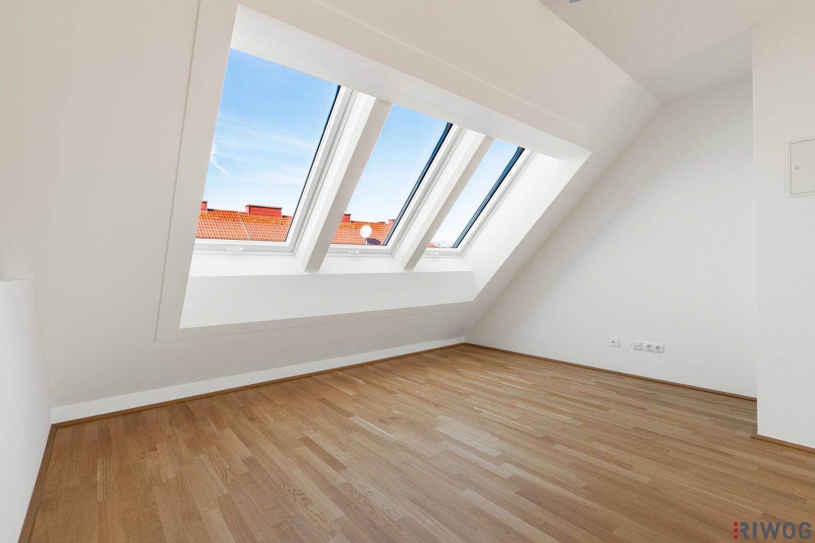 Heller Wohnraum mit Holzboden, Dachschrägen und großen Dachfenstern für viel Tageslicht.