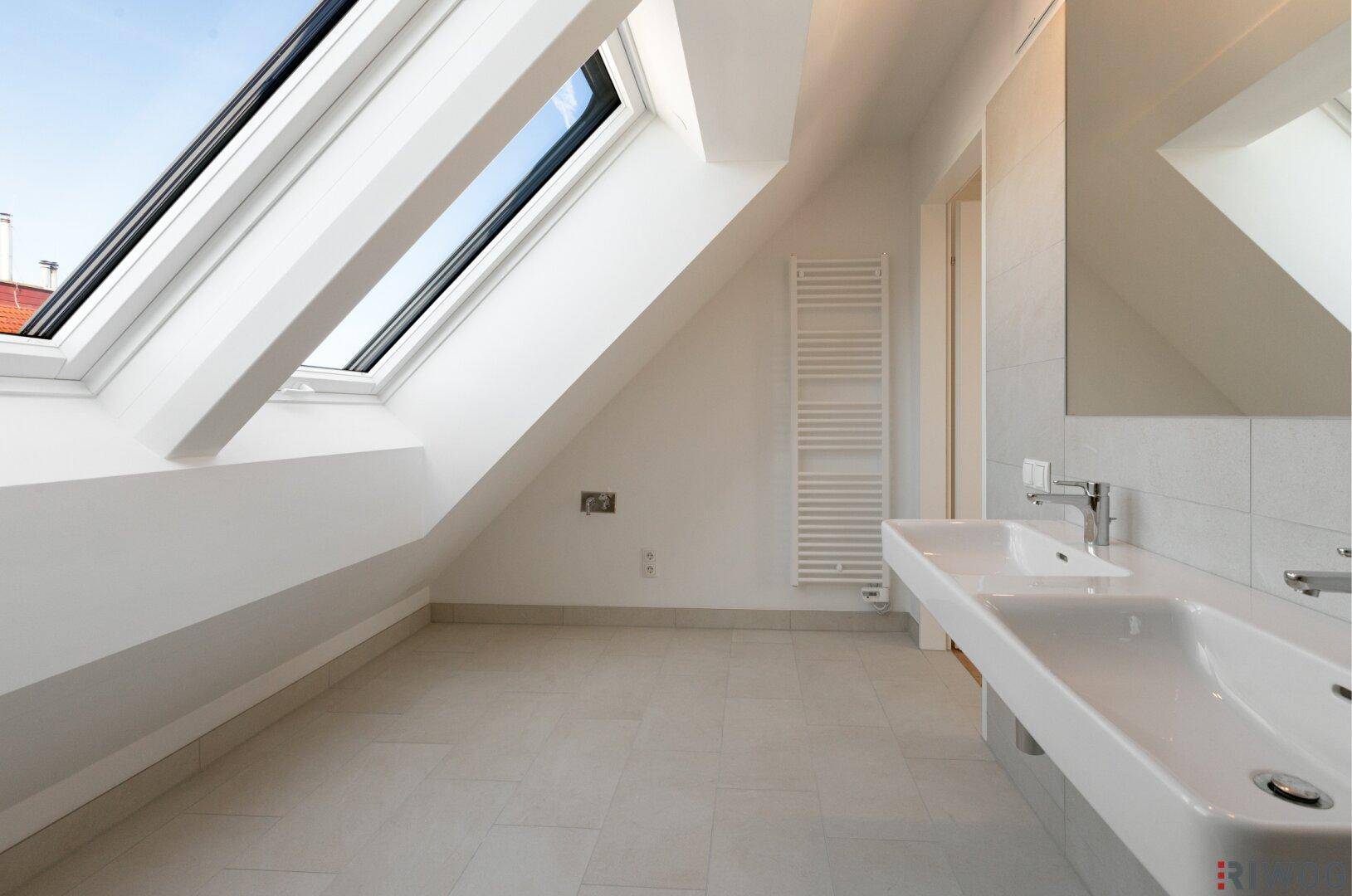 Helles Badezimmer mit Doppelwaschbecken, Fliesenboden und Dachfenstern für Tageslicht.