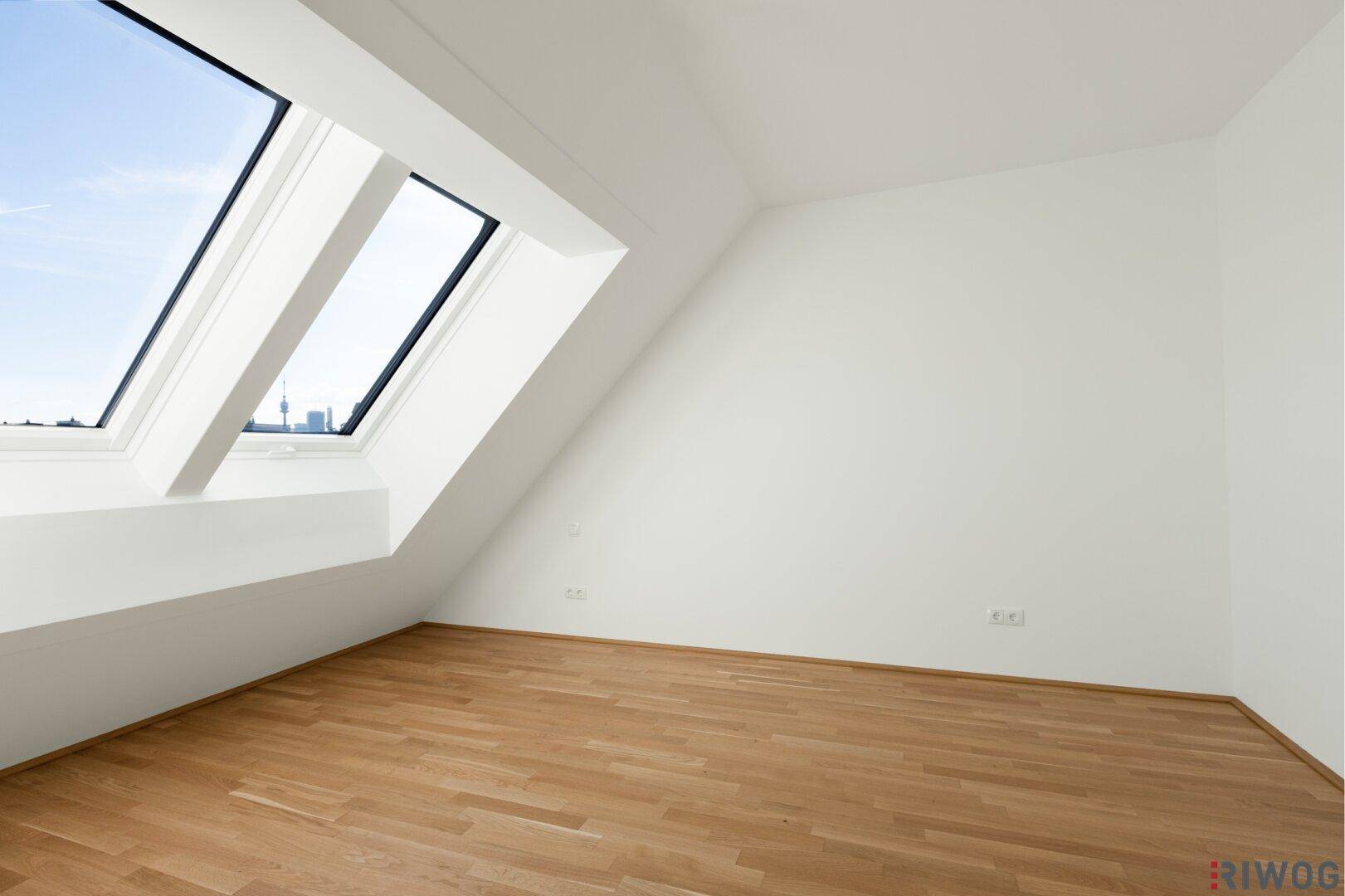 Helles Schlafzimmer mit Holzboden, Dachschrägen und großen Dachfenstern mit Stadtblick.