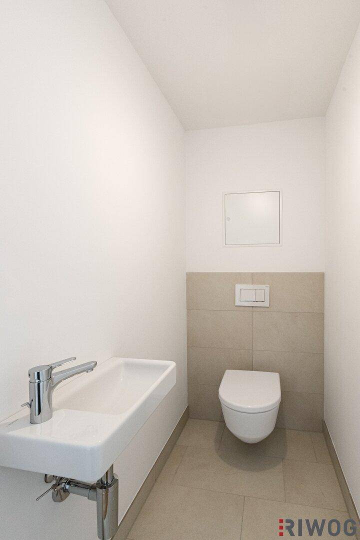 Modernes Gäste-WC mit Wand-WC, kleinem Waschbecken und beigefarbenen Fliesen.