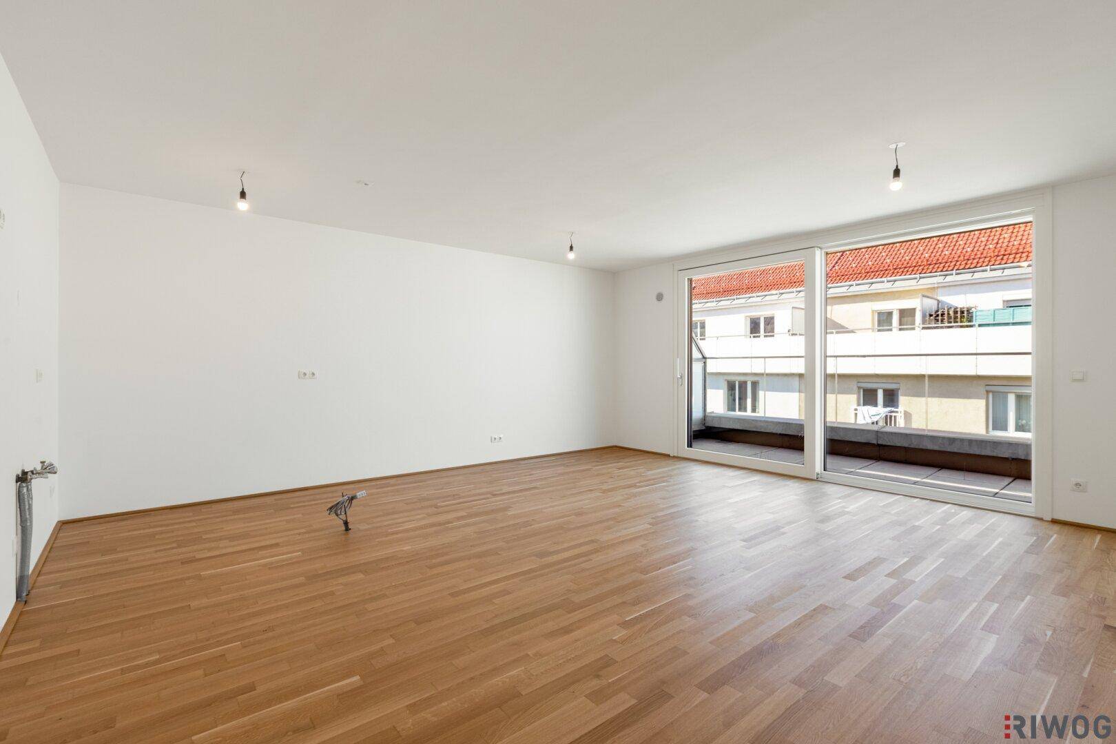 Geräumiges, leeres Wohnzimmer mit Parkettboden und großzügigem Zugang zum Balkon.