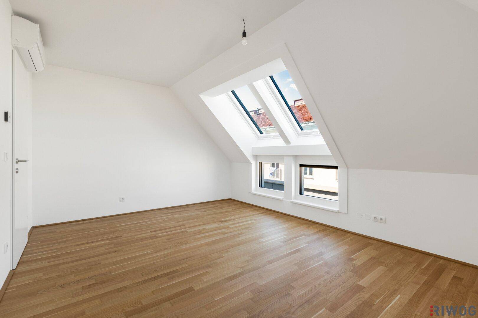 Dachgeschosszimmer mit Parkettboden, Klimaanlage und hellen Dachfenstern, bereit zur Einrichtung.